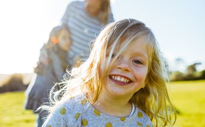 Young blonde girl running forwards with her mother and sister on a grass hill